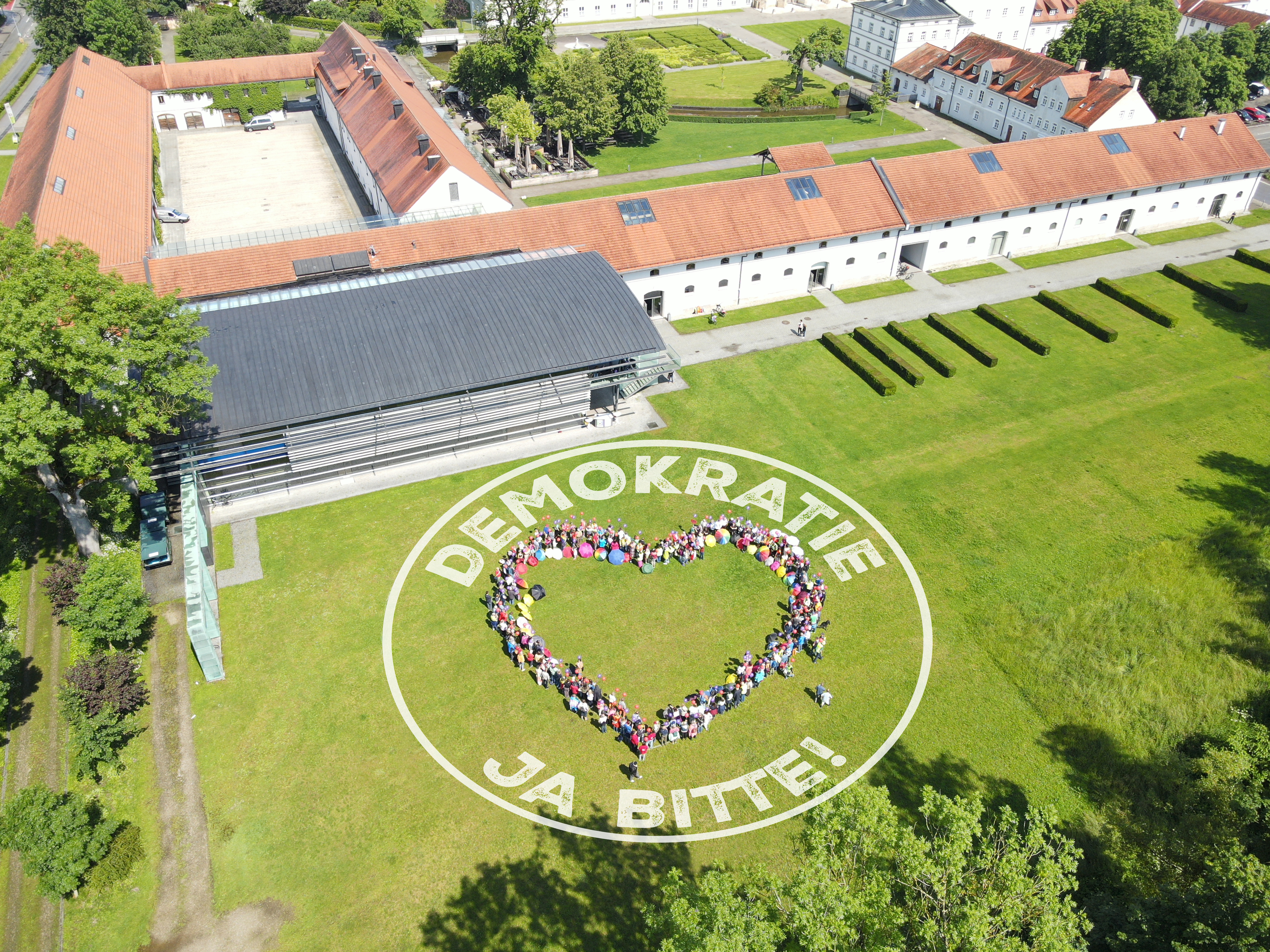 Luftbild zeigt Gruppe von Menschen, die ein Herz formen. Das Logo von Bündnis für Demokratie